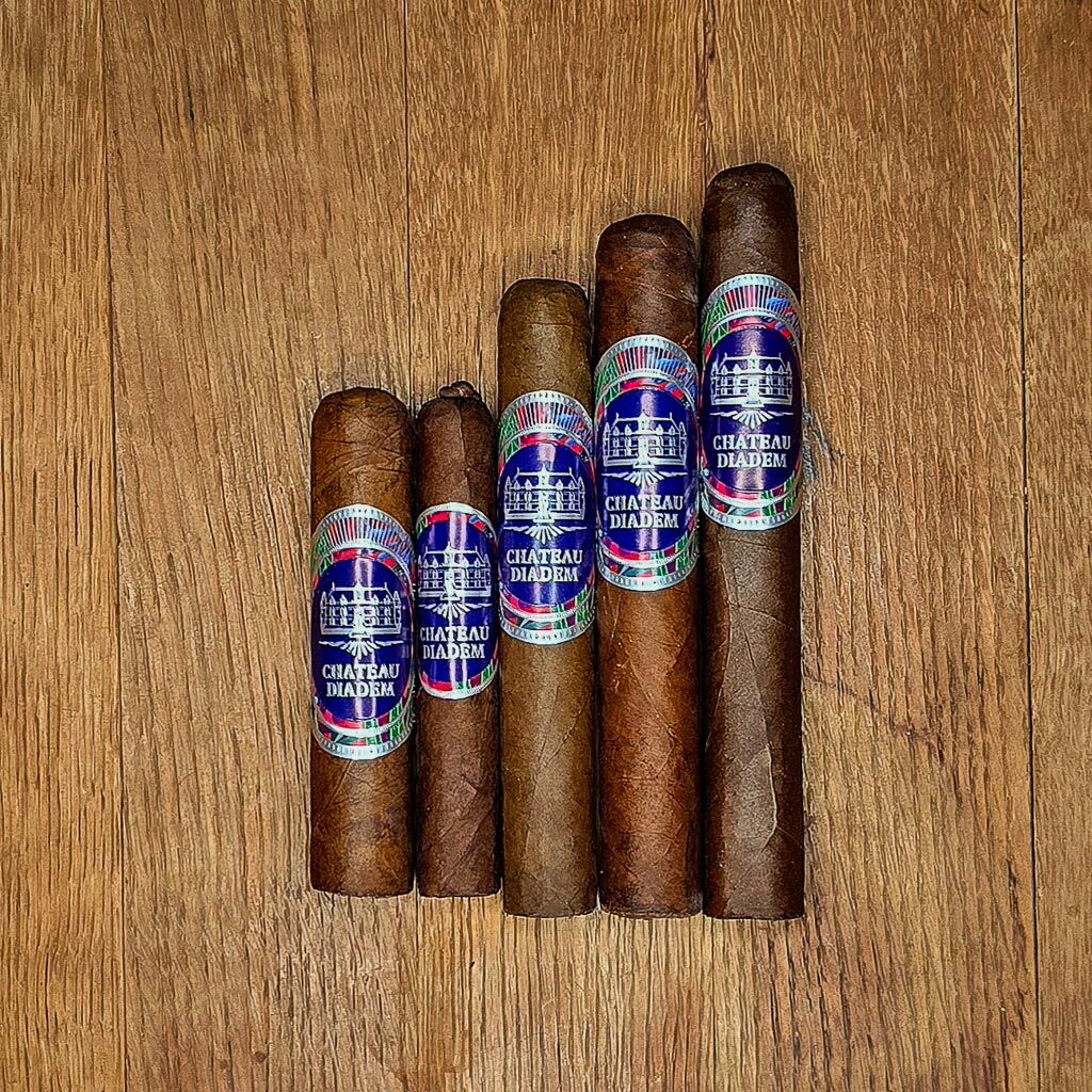 Five Chateau Diadem Certitude vitolas displayed in graduated size order on rustic wood surface showing Ecuadorian Habano wrapper and signature blue and multicolor band at Smokers Abbey Austin