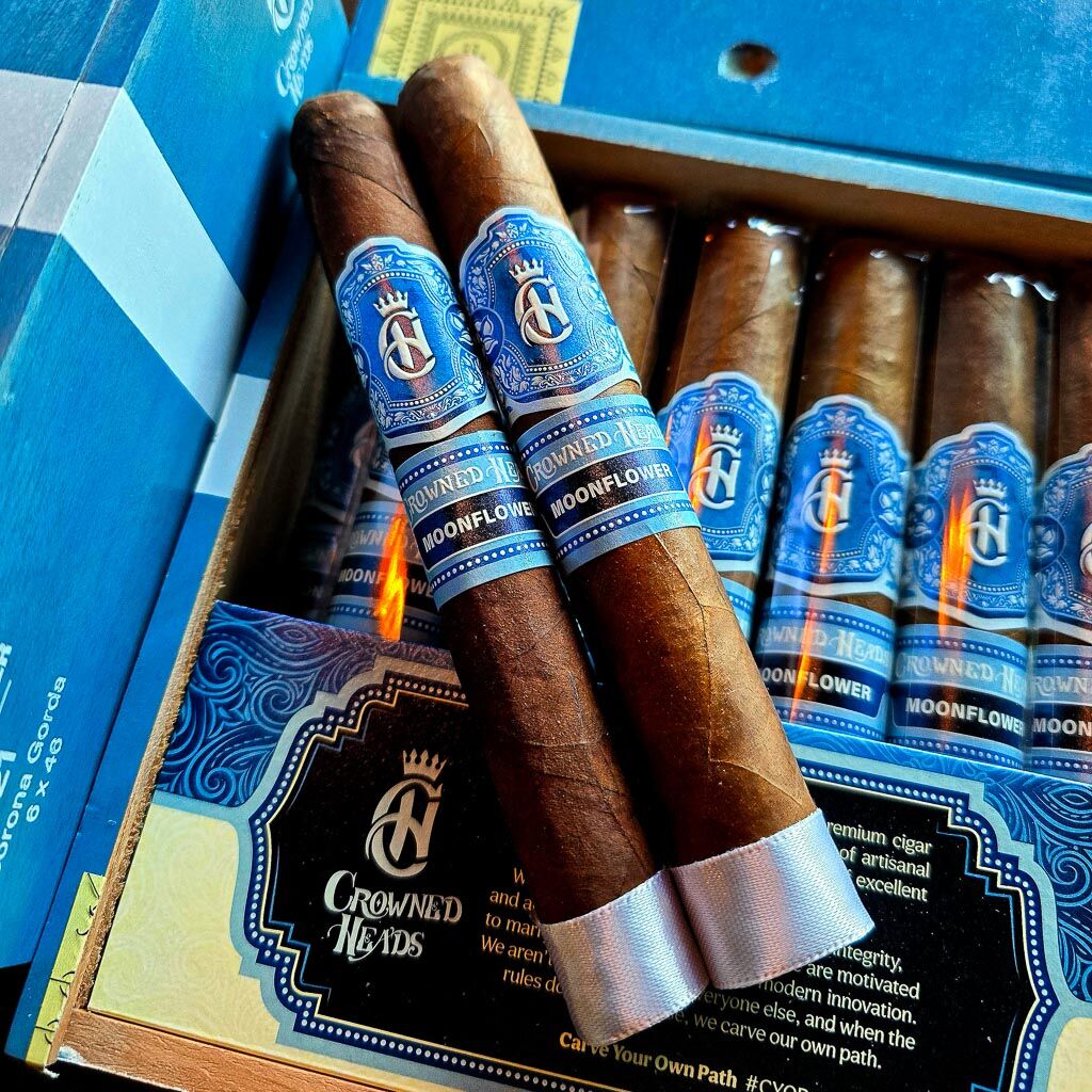 Two Crowned Heads Moonflower cigars resting on open 21-count box with Carve Your Own Path brand card visible showing Nicaraguan Corojo wrapper and blue and gold Moonflower band at Smokers Abbey Austin