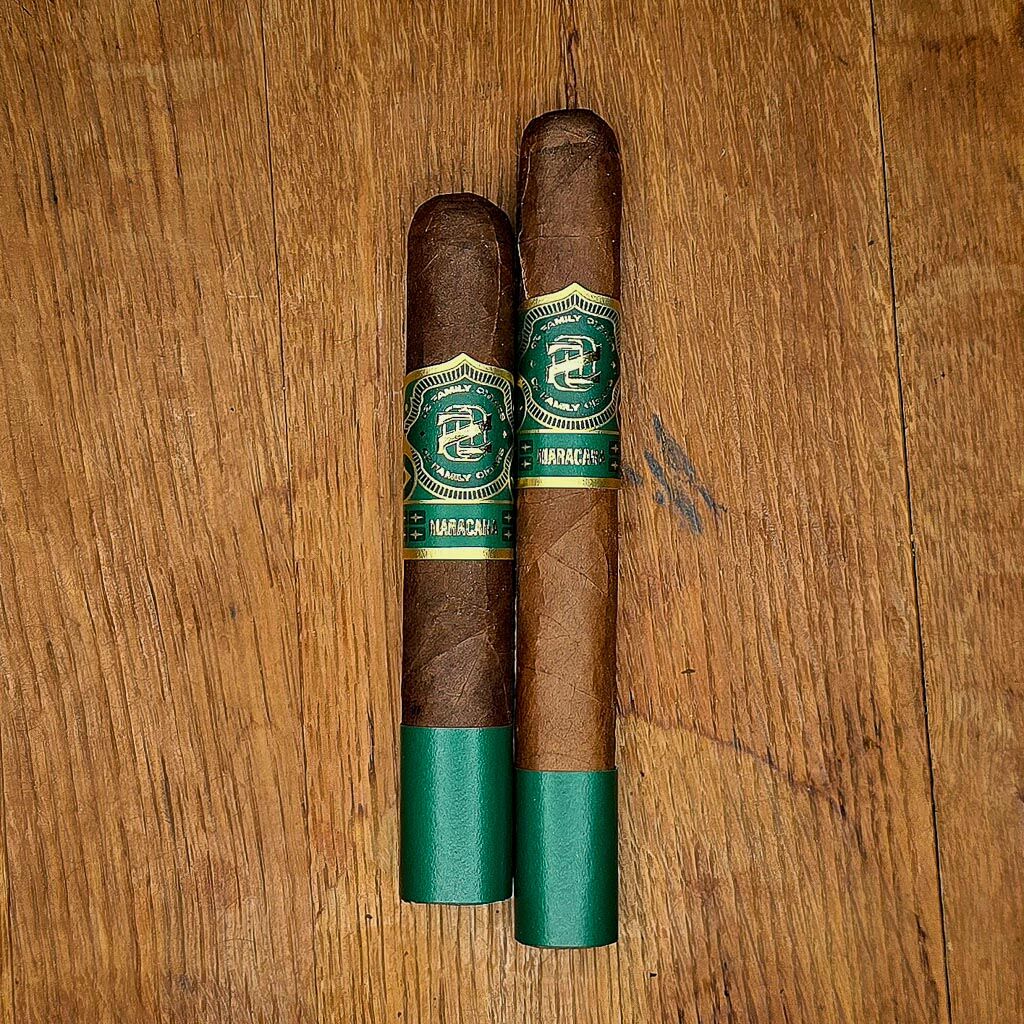 Ozgener Maracana Box Pressed Robusto Extra and Toro cigars displayed side by side on rustic wood surface showing Brazilian Arapiraca wrapper and green and gold OZ Family Cigars Maracana band at Smokers Abbey Austin