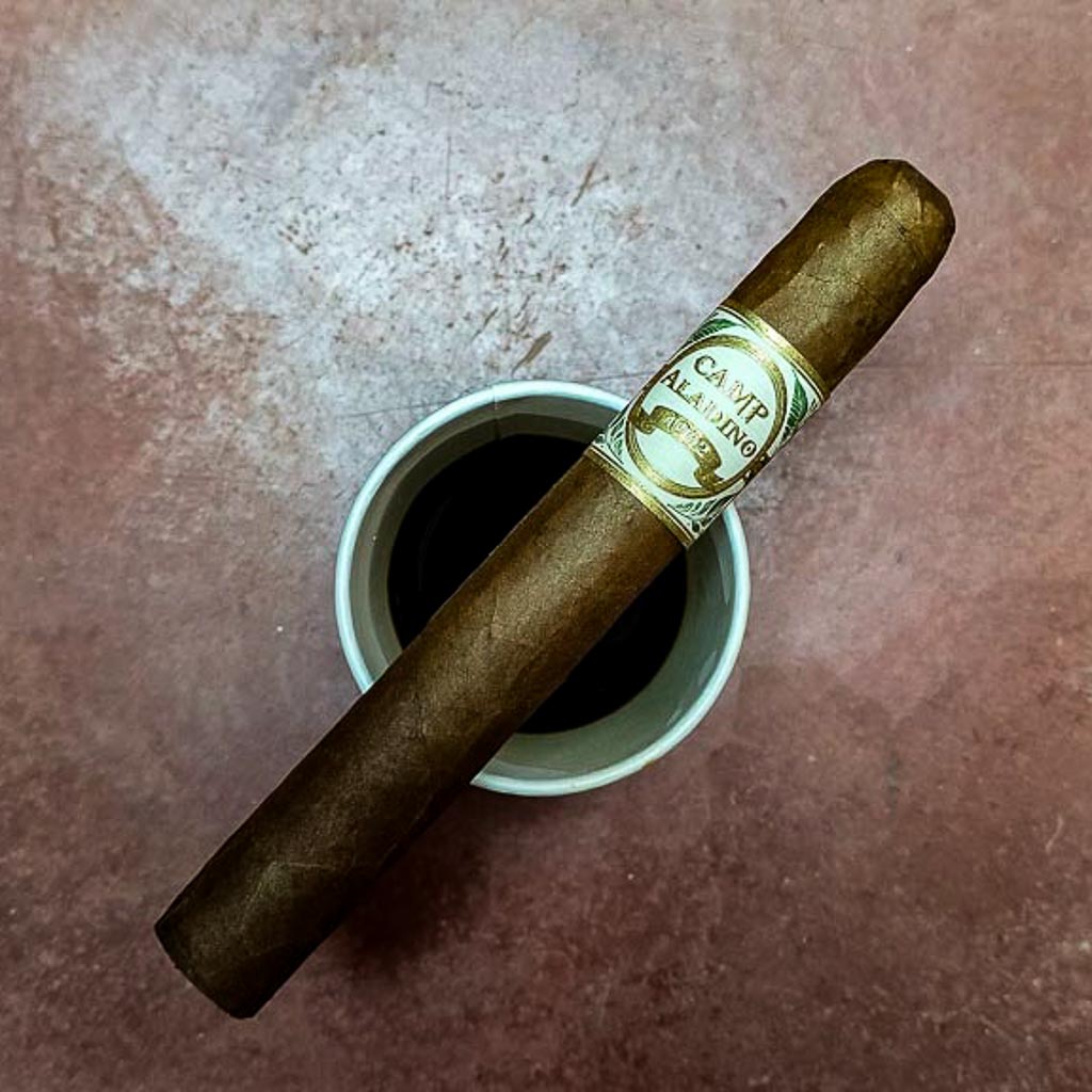 JRE Aladino Camp Aladino 1962 Toro cigar resting across a small cup on a terracotta tile surface showing the white and gold Camp Aladino 1962 band at Smokers Abbey Austin