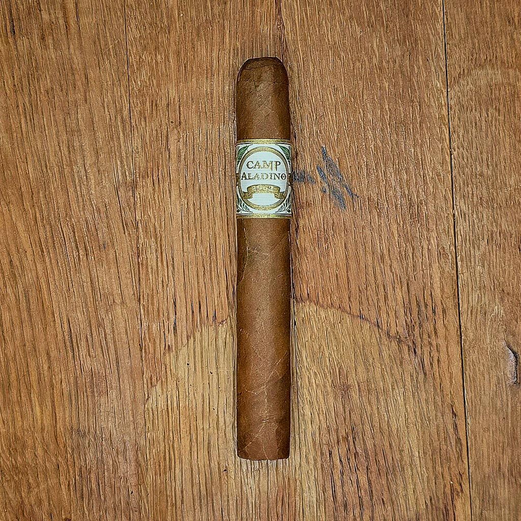 JRE Aladino Camp Aladino 1962 Toro cigar displayed on rustic wood surface showing Honduran wrapper and white and gold Camp Aladino 1962 band at Smokers Abbey Austin