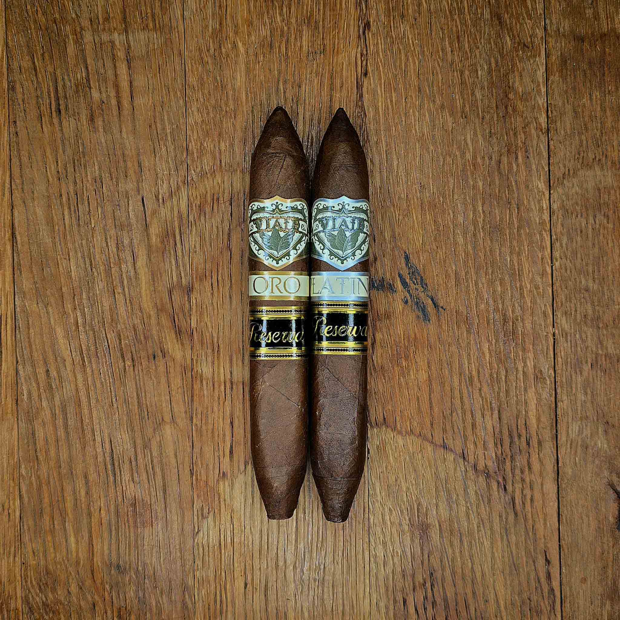 Viaje Perfecto Reserva Oro and Platino cigars displayed side by side on rustic wood surface at Smokers Abbey Austin