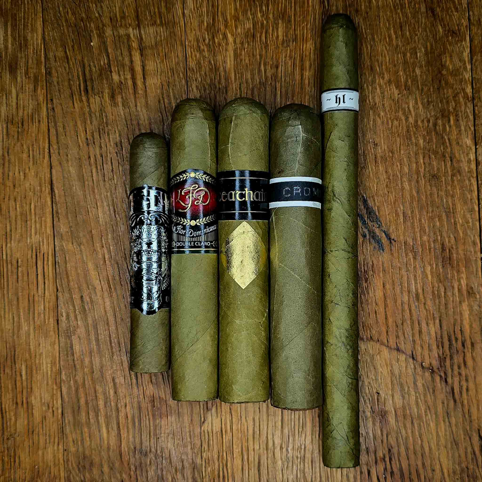 Candela No.2 Sampler featuring five candela-wrapped cigars including Little Green One and Cavalier Genève Ceathair, displayed side by side on rustic wood at Smokers Abbey Austin
