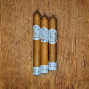 Three Black Label Trading Co. Porcelain cigars with elegant white and silver Deliverance band displayed on rustic wood surface at Smokers Abbey Austin