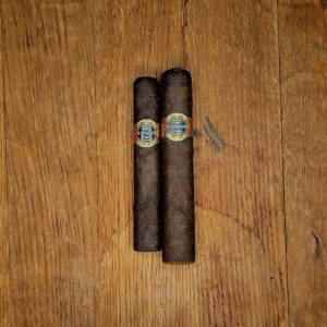 Two Warped Corto Maduro box pressed cigars resting on wooden surface showing dark Mexican San Andrés wrapper and ornate Corto band.