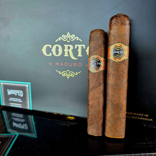 Warped Corto Maduro cigars positioned in front of black Corto Maduro box displaying box pressed shape and band detail.