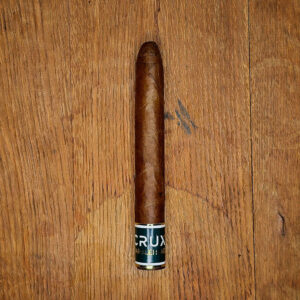 Single Crux Marblehead Toro cigar with rounded 109 cap resting on wooden surface, showing foot band and Colorado Habano wrapper.