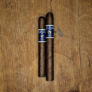 Two Crux Passport cigars with blue and gold bands resting on a wooden surface, featuring Ecuadorian Habano wrapper.