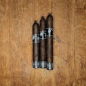 Three BLTC Macabre limited release cigars in Robusto, Corona Gorda, and Toro vitolas displayed side by side on rustic wood surface showing dark Mexican San Andrés wrapper and black and silver Macabre band at Smokers Abbey Austin