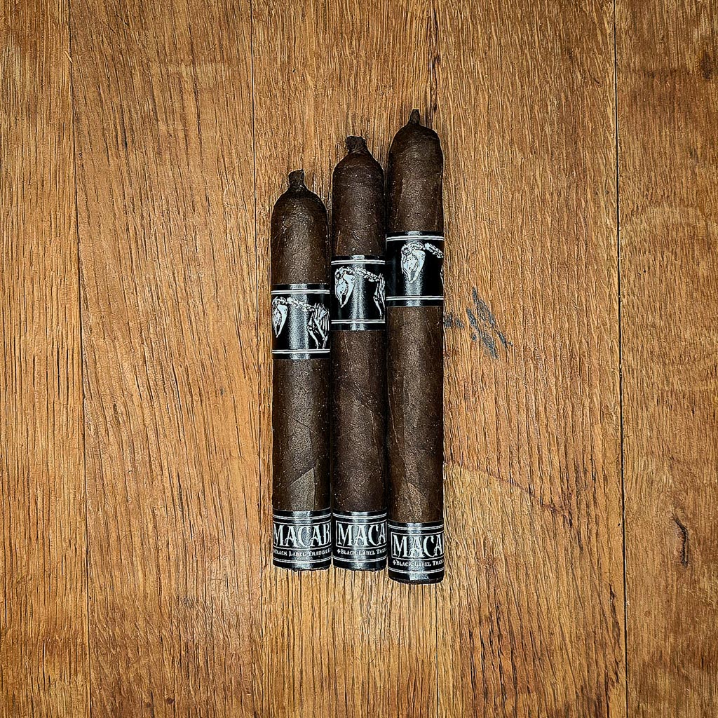 Three BLTC Macabre limited release cigars in Robusto, Corona Gorda, and Toro vitolas displayed side by side on rustic wood surface showing dark Mexican San Andrés wrapper and black and silver Macabre band at Smokers Abbey Austin
