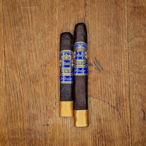 Casa Carrillo Pledge Prequel and Sojourn box pressed cigars with blue and gold band and gold footer displayed side by side on rustic wood surface at Smokers Abbey Austin