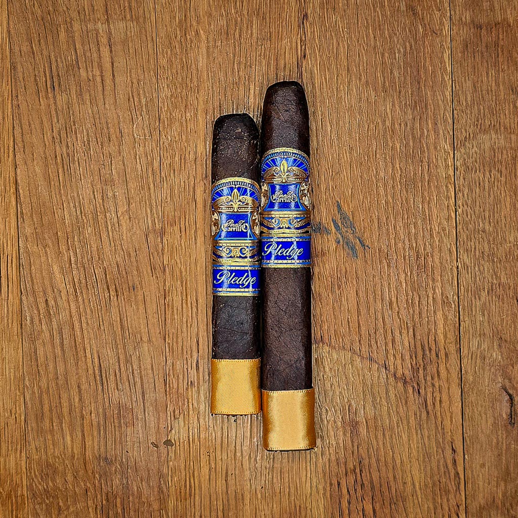 Casa Carrillo Pledge Prequel and Sojourn box pressed cigars with blue and gold band and gold footer displayed side by side on rustic wood surface at Smokers Abbey Austin