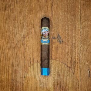 El Mago Beach Blend box pressed robusto cigar with blue footer band and colorful El Mago Est. 1965 band displayed on rustic wood surface at Smokers Abbey Austin