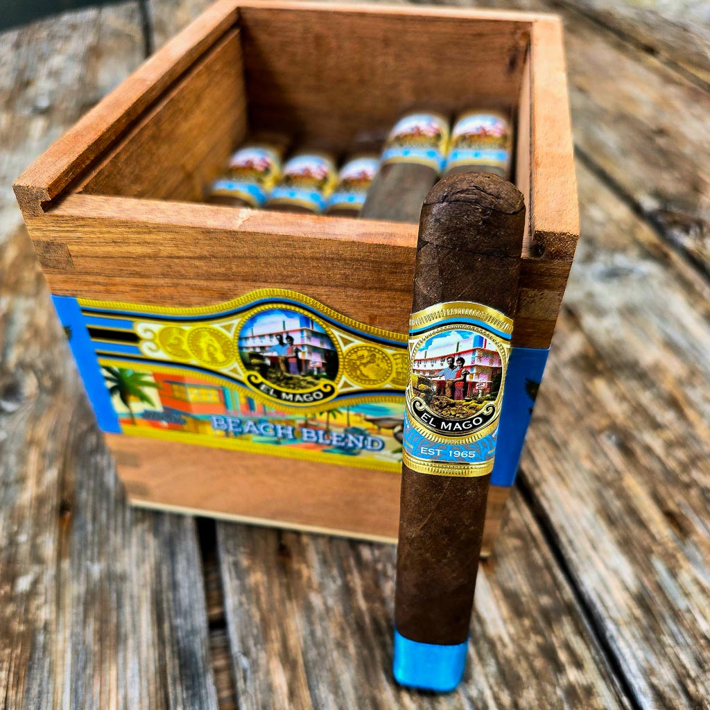 El Mago Beach Blend box pressed robusto leaning against an open 25-count wooden bundle box with colorful Beach Blend box art visible on outdoor wood surface at Smokers Abbey Austin