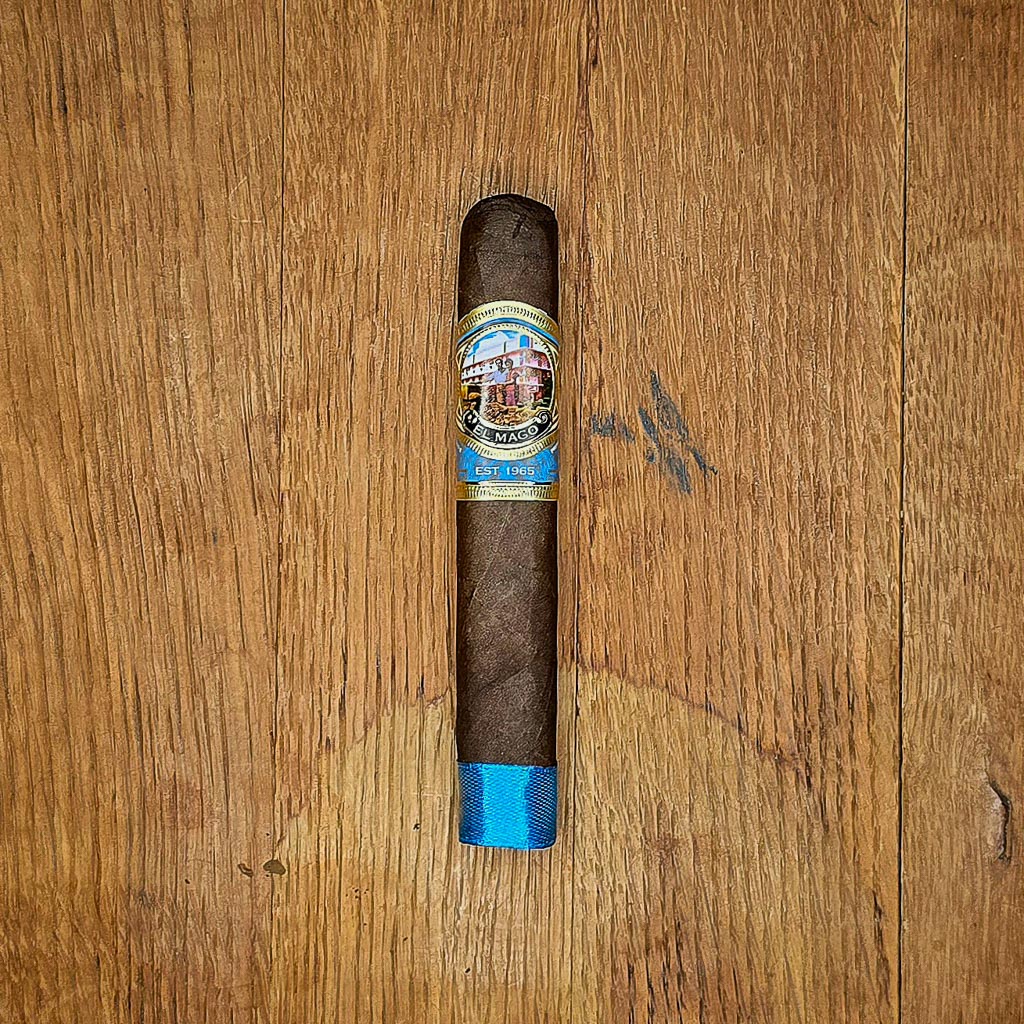 El Mago Beach Blend box pressed robusto cigar with blue footer band and colorful El Mago Est. 1965 band displayed on rustic wood surface at Smokers Abbey Austin