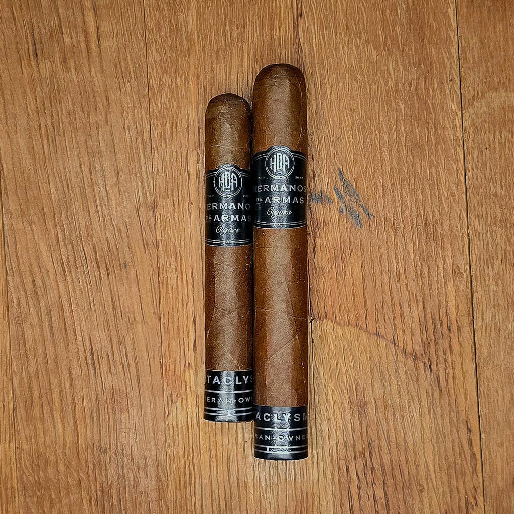 Hermanos De Armas Cataclysm Robusto and Toro cigars displayed side by side on rustic wood surface showing Ecuadorian Habano wrapper and black HDA band with Cataclysm Veteran-Owned footer at Smokers Abbey Austin