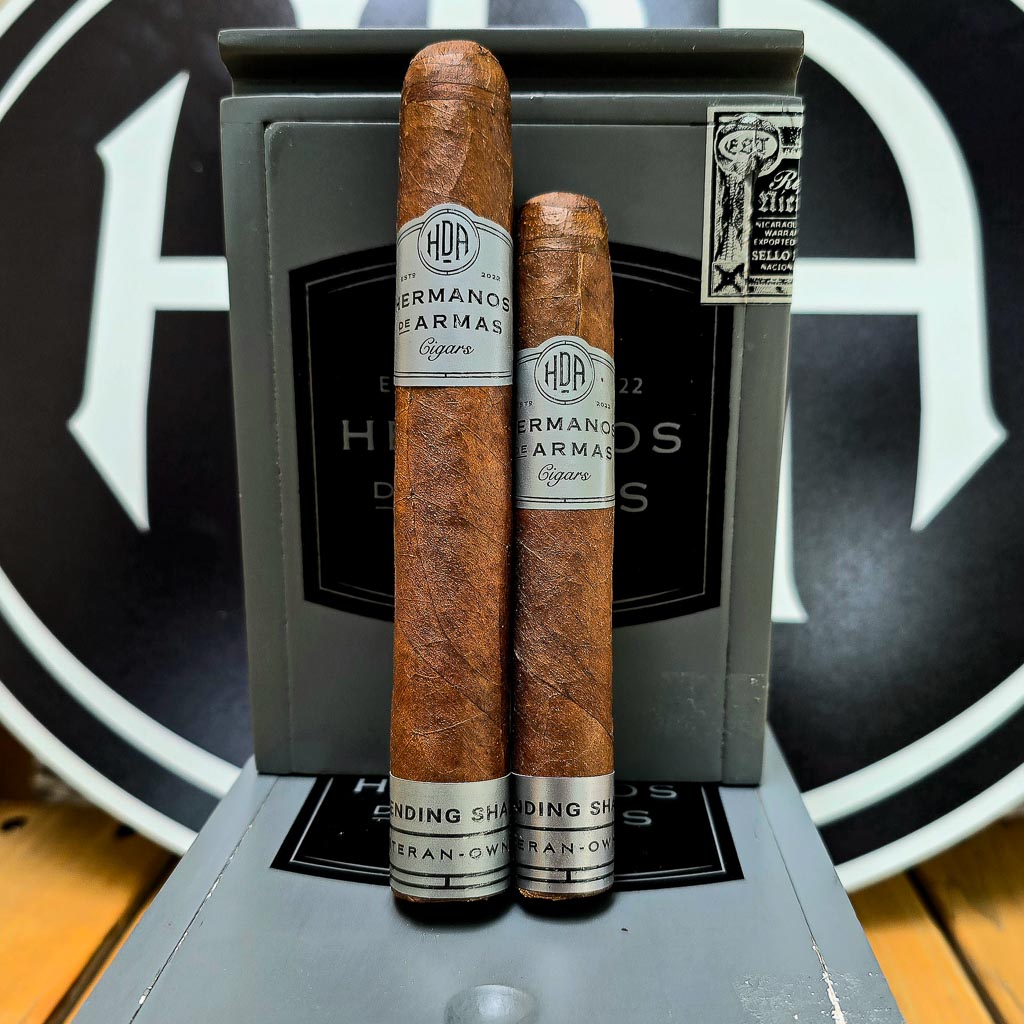 Hermanos De Armas Descending Shadows Robusto and Toro cigars displayed side by side on rustic wood surface showing Ecuadorian Sun Grown wrapper and silver HDA band with Descending Shadows Veteran-Owned footer at Smokers Abbey Austin