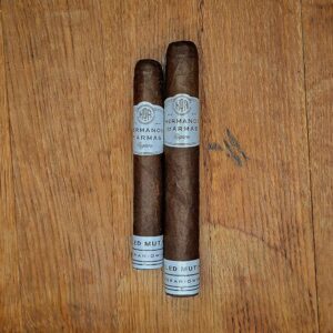 Hermanos De Armas Veiled Mutiny Robusto and Toro cigars displayed side by side on rustic wood surface showing Ecuadorian Maduro wrapper and white HDA band with Veteran-Owned footer at Smokers Abbey Austin