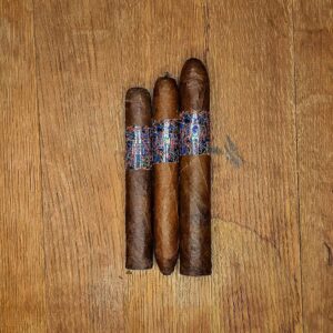 hree La Instructora Perfección cigars in Petite Salomón, Royal Corona, and Belicoso Extra vitolas displayed side by side on rustic wood surface showing Ecuadorian Habano Rosado wrapper and holographic multicolor band at Smokers Abbey Austin