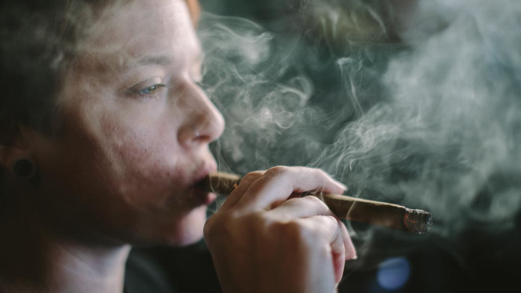 Woman smoking a cigar with smoke billowing, highlighting a slow and intentional smoking experience