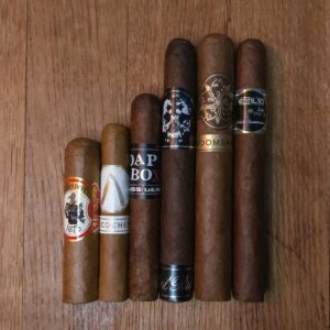 Ecuador Bold Side cigar sampler featuring Lampert Rojo, La Barba Ricochet Cru Shade, Dissident Soapbox, BLTC Last Rites, Room 101 Passive, and Emilio AF2 displayed side by side on rustic wood surface at Smokers Abbey Austin