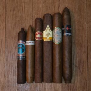 Ecuador Full Spectrum cigar sampler featuring Emilio Cavatina, RoMa Craft Intemperance EC, Crowned Heads Four Kicks, Artista Harvest, Patina Habano, and L'Atelier Surrogates 7th Sam displayed side by side on rustic wood surface at Smokers Abbey Austin
