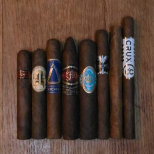 Short Format No. 2 cigar sampler featuring Illusione 68 Maduro, Caldwell The King Is Dead Manzanita, La Barba Mexi Sol, LFD Oscuro Torpedo, Crowned Heads La Imperiosa Magicos, BLK WKS Rorschach Petite Panatela, Crux Du Connoisseur No. 3, and Artista Fugly displayed on rustic wood surface at Smokers Abbey Austin