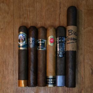 Biggie cigar sampler featuring El Mago Disco, Room 101 Big Payback Maduro Gordo, Emilio AF1 Gran Toro, HVC Hot Cake Golden Line Gordo, OSOK San Andrés Puro Gordo, and Oscar Valladares Big Johnny displayed side by side on rustic wood surface at Smokers Abbey Austin