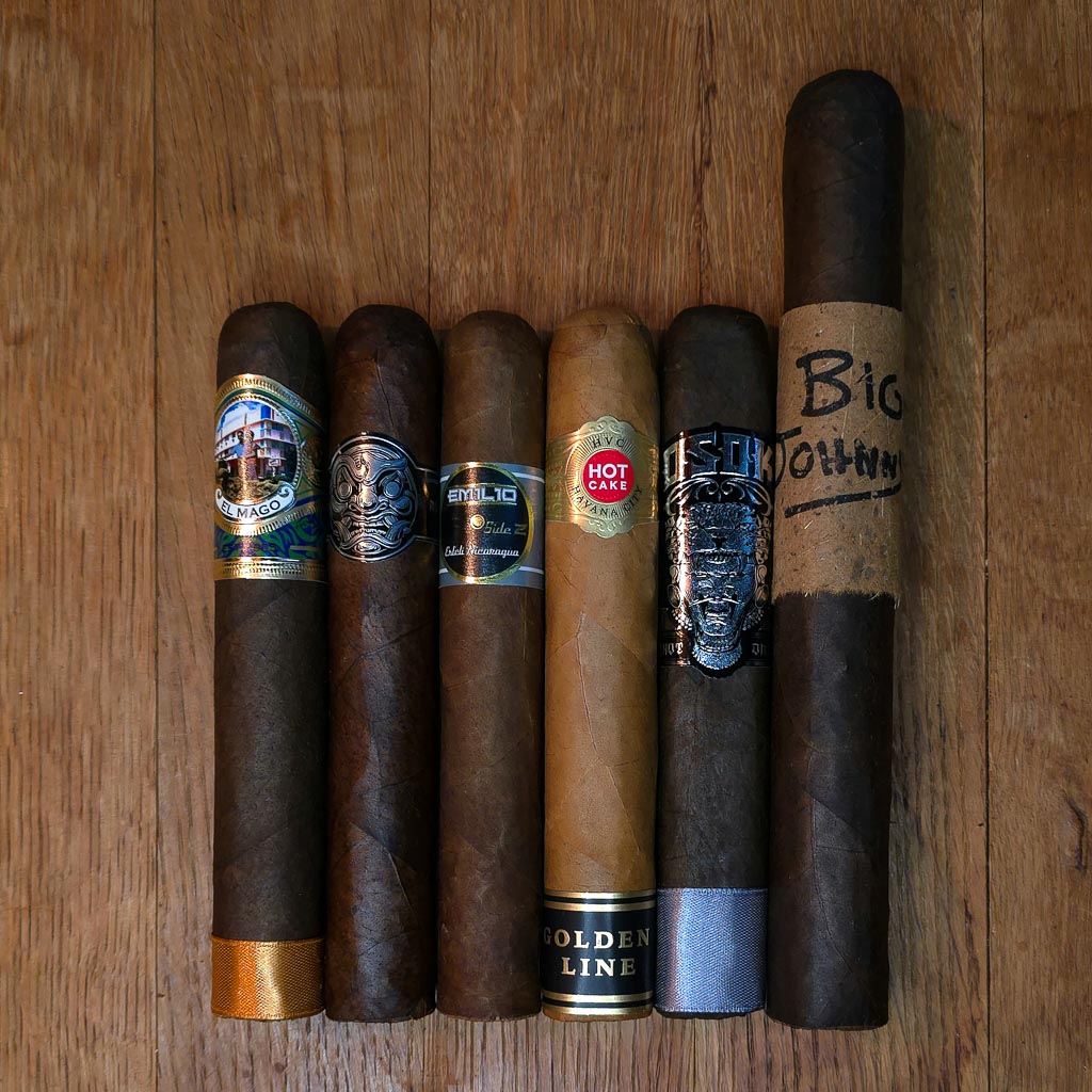 Biggie cigar sampler featuring El Mago Disco, Room 101 Big Payback Maduro Gordo, Emilio AF1 Gran Toro, HVC Hot Cake Golden Line Gordo, OSOK San Andrés Puro Gordo, and Oscar Valladares Big Johnny displayed side by side on rustic wood surface at Smokers Abbey Austin