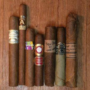 Honduras cigar sampler featuring JRE Aladino Camp Aladino 1962 Toro, Aladino Vintage Selection Elegante, Cavalier Genève Tres Delincuentes, Cavalier Domaine Rouge, Oscar Valladares Raw Dog, The Oscar Maduro Robusto, and Leaf By Oscar Sumatra displayed on rustic wood surface at Smokers Abbey Austin