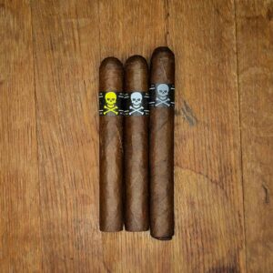 Viaje Skull and Bones Ghost Rider three cigars with yellow, white, and silver skull and crossbones bands displayed side by side on rustic wood surface at Smokers Abbey Austin