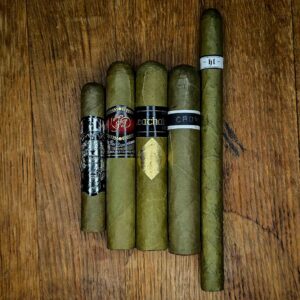 Candela No.2 Sampler featuring five candela-wrapped cigars including Little Green One and Cavalier Genève Ceathair, displayed side by side on rustic wood at Smokers Abbey Austin