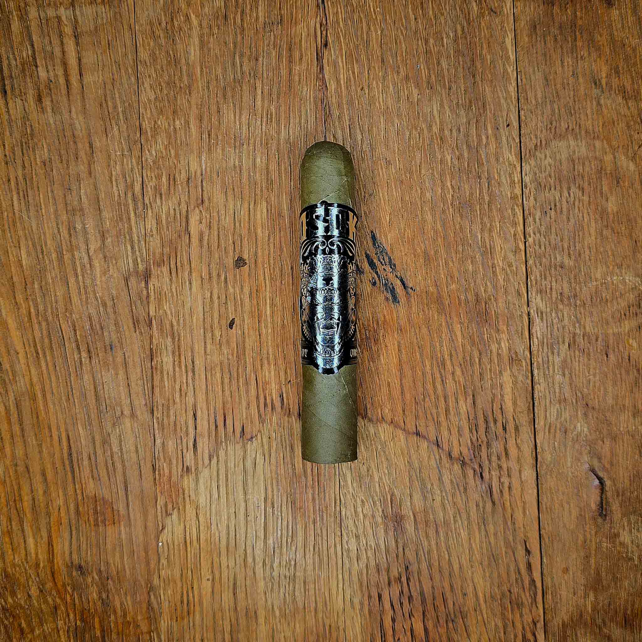 Little Green One candela cigar with black OSOK band featuring a roaring jaguar illustration, displayed on rustic wood surface at Smokers Abbey Austin