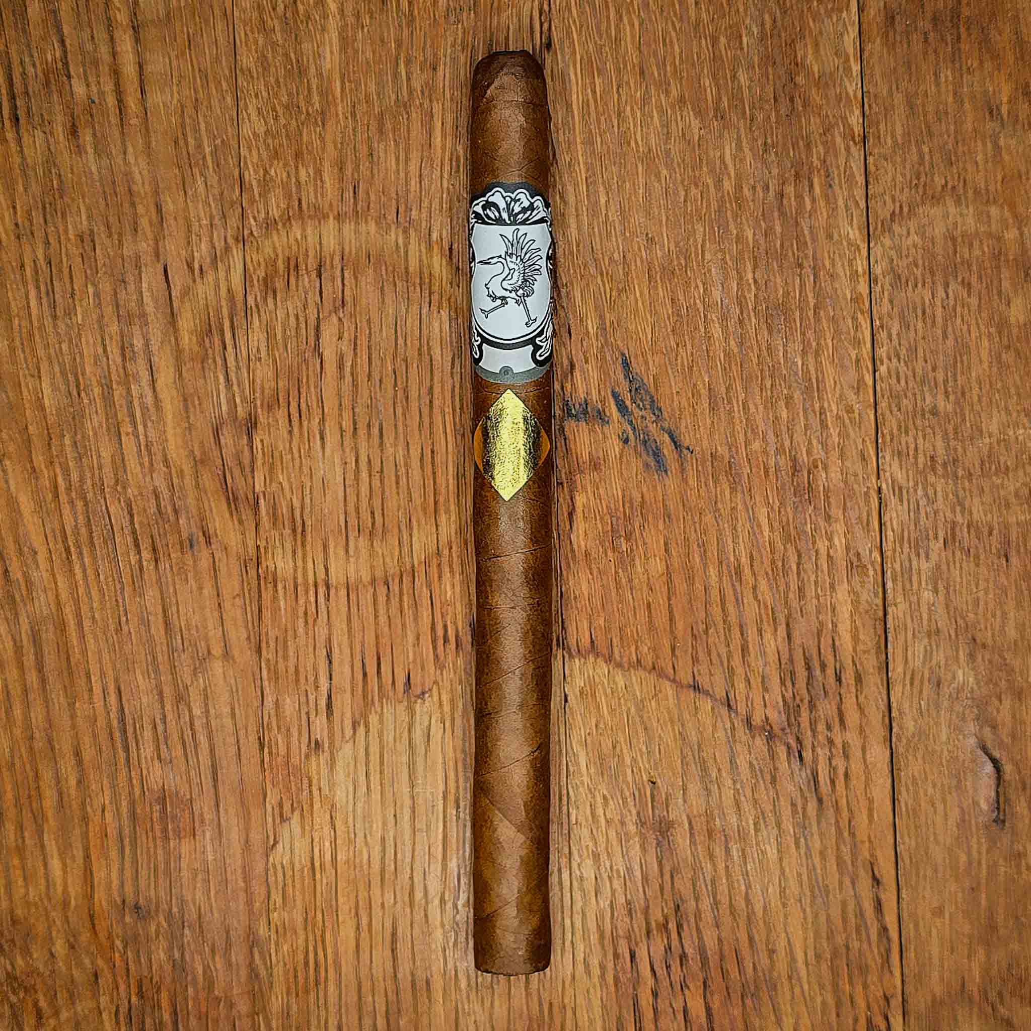 Cavalier Genève Small Batch Lancero with white crest band and gold diamond foil badge on a rustic wood surface at Smokers Abbey Austin